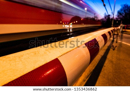 A closed railway barrier in germany with a train in motion and cars waiting