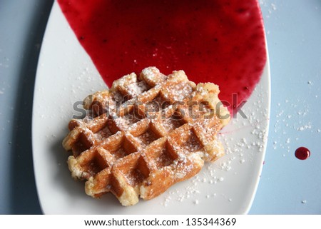 A belgian waffle with sugar icing and red cherry sauce