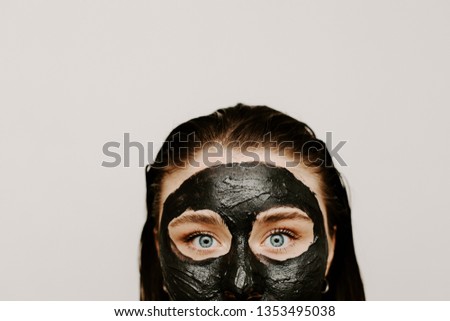 Cut view of portrait young woman wearing black facial treatment mask. Looking straight. Isolated on grey background