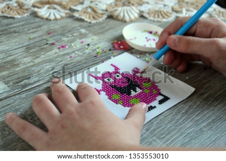 The process of making a picture of a decorative diamond mosaic, the hands of the girl hold a special tool for capturing the mosaic, handmade, selective focus.