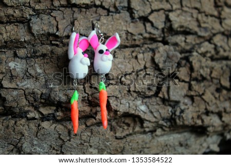 Hanging earrings in the form of Easter rabbits with carrots on a piece of wooden bark, selective focus.