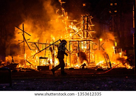 Silhouette of fireman trying to control a fire in a street during a night.