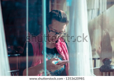 A woman in glasses in a cafe looks into the phone. Photo behind the glass.