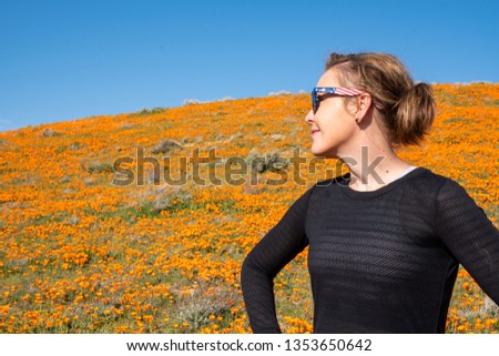 Happy woman smiles off into the distance looking at the bright orange hills filled with poppies during the superbloom at Antelope Valley Poppy Reserve in California