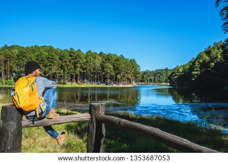 Young men travel in nature in the mountains, with lakes, beautiful ponds. Traveler with backpack standing on top Of the lake viewpoint, tourism to relax during the holidays.