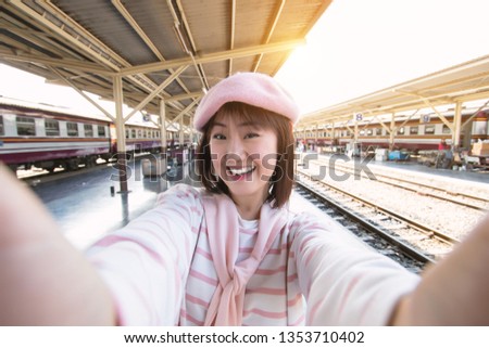 Closeup of young attractive beautiful woman holding smartphone digital camera with her hands taking selfie on summer holiday in train station.