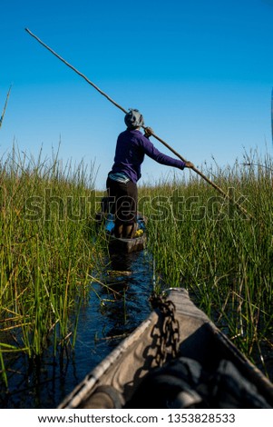 Series of unrecognisable people on mokoro or canoe safari on the okavango delta in Botswana Africa with blue sky and green reeds water reflection