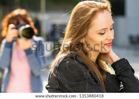 Happy woman having portrait photo shoot. Young adult female and photographer paparazzi taking pictures in background.
