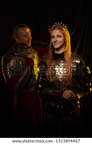 Blonde queen girl and a male knight in medieval armor 15th century in yellow light against a dark background