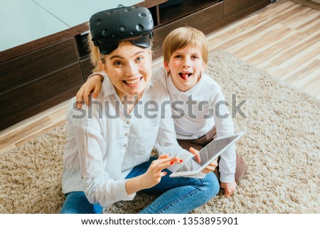 Mother with virtual reality headset and son sitting on floor using digital tablet. Happy mom and little boy using tablet with touchscreen watching a video. Smiling sister and brother playing on tablet