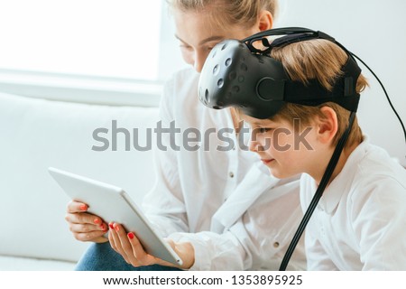 Mother and son with virtual reality headset sitting onsofa using digital tablet. Happy mom and little boy using tablet with touchscreen watching a video. Smiling sister and brother playing on tablet