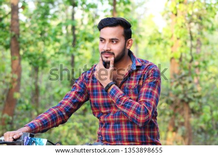 young man model touching his face and sitting on a bike in the forest
