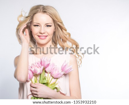 The girl with bright makeup holds a bouquet of pink tulips. Studio portrait. Spring bouquet in the hands of fragile blonde