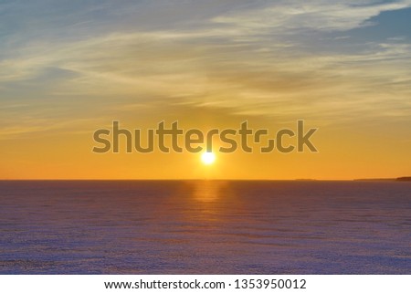 The sunset or sunrise. The cloudy sky cloured in red, orange, crimson, purple, violet and blue bright and vivid coloures with setting or rising sun over the sea, lake or bay covered with ice and snow