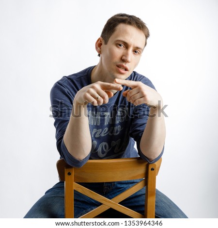 A young guy sits on a chair and emotionally talks on a white background. Interview, casting, monologue.