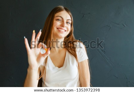 Longhaired teen woman in white t-shirt showing gesture ok and laughing while standing on the gray background