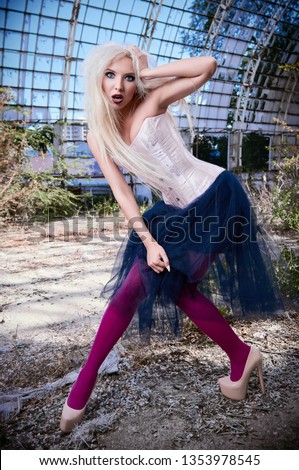 Portrait of the beautiful shocked (confused) freak girl. Attractive weird woman wearing corset, tights and tutu skirt in abandoned place. Odd fashion


