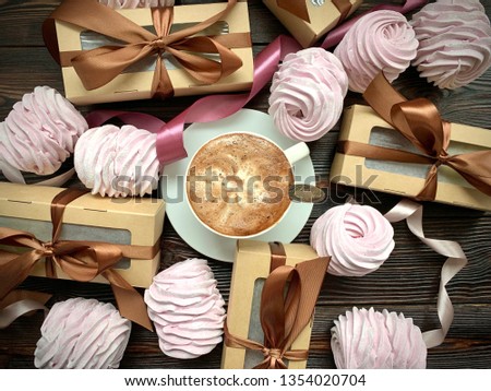 On a dark background: coffee with foam, pink marshmallows, Zephyr  - gifts with bows, green flowers.