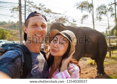 Travel, summer and holiday concept - Lovely couple taking selfie near palm trees and elephant.