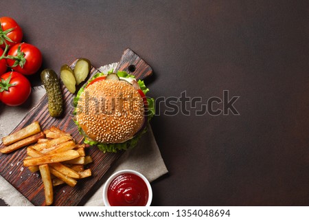 Homemade hamburger with ingredients beef, tomatos, lettuce, cheese, onion, cucumbers and french fries on cutting board and rusty background. Top view with place for your text.
