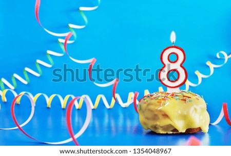 Birthday of eight years. Cupcake with white burning candle in the form of number 8. Vivid blue background with copy space