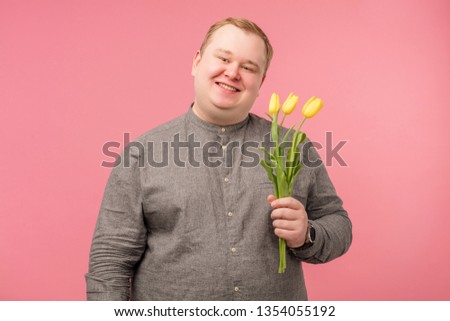 Caucasian softie tubby man holding yellow tulips while thinking ready for Valentine day, isolated on pink background