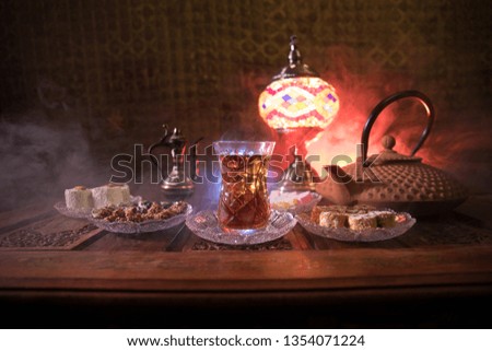 Arabian tea in glass with eastern snacks on vintage wooden surface. Eastern tea concept. Low light lounge interior with carpet. Empty space. Selective focus.