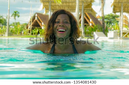 young happy and beautiful black African American woman in bikini having fun at tropical beach resort swimming pool relaxed and playful smiling cheerful enjoying summer holidays luxury travel