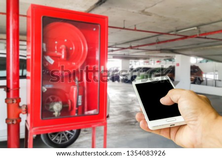 Man use mobile phone, blur image of fire extinguisher in the parking building as background.