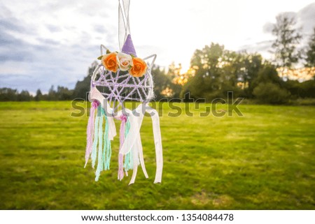 Colorful dreamcatcher outdoors on summer nature background. Handmade decor made of feathers, ribbons, threads and beads.