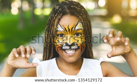 Funny little tiger. Adorable african-american girl with creative face painting roaring, playing wild cat outdoors Royalty-Free Stock Photo #1354129172