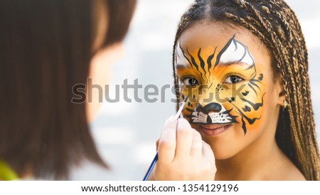 Adorable african-american girl getting tiger face painting in park, empty space Royalty-Free Stock Photo #1354129196