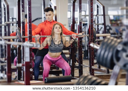 young girl doing squats with a barbell in the gym under the supervision of a trainer, healthy lifestyle
