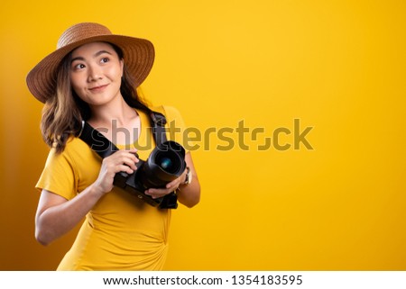 Woman in summer hat standing with photo camera isolated over yellow background