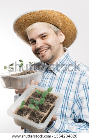 cheerful farmer in a plaid shirt and cowboy hat is holding spring seedlings in peat biodegradable pots. agronomist studying young seedlings of cucumbers. Baby plants seeding