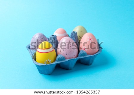 Colorful Easter eggs in carton tray on blue background. Minimal concept.