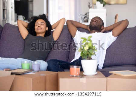 African couple put hands behind head rest on sofa with closed eyes big boxes with stuff, breath fresh air take break on moving day into new first home. Property buyers or easy delivery service concept Royalty-Free Stock Photo #1354297115