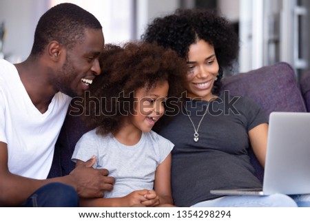 African couple preschool daughter spend weekend together sitting on couch use computer make video call shopping online watching funny video cartoons free time family leisure activities at home concept