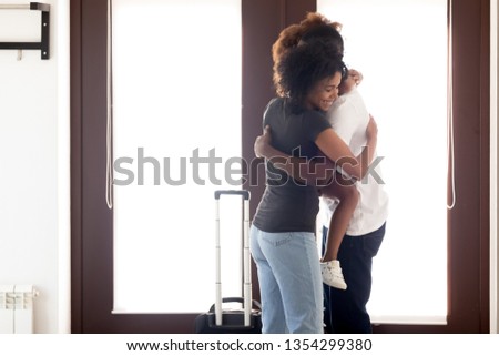 African family standing embracing at hallway meet father after long business trip, wife daughter feels happy hug daddy, husband arrived returning at home, girls miss, welcome back and reunion concept