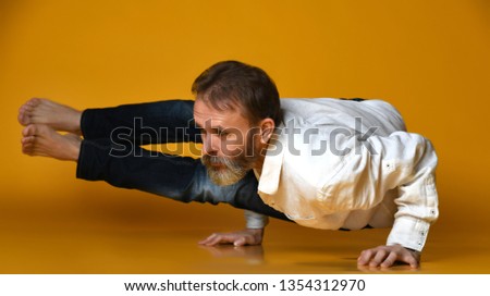 bearded man practicing yoga doing stretching exercises dressed casually in shirt and jeans, against orange background