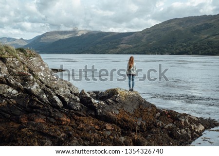 A girl looks at the horizon from the lake at the side of Eilean Donan Castle in Scotland.