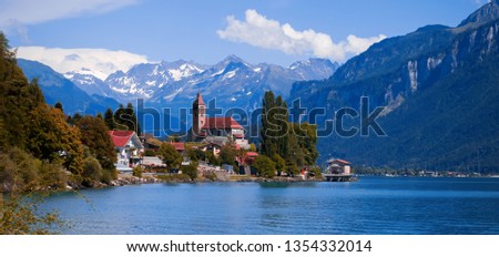 Panoramic view on the Brienz town on lake Brienz by Interlaken, Switzerland. Old fishing town with beautiful church and snow covered blue Alps mountains on background. Switzerland, Bohemia, Europe. Royalty-Free Stock Photo #1354332014