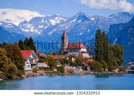  Old fishing town with beautiful church and fabulous snow covered Alps mountains on background. Panoramic view on Brienz town on lake Brienz by Interlaken, Switzerland. Switzerland, Bohemia, Europe. Royalty-Free Stock Photo #1354332953