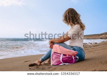 girl in tight jeans barefoot with pink bag shopper in hand on sandy beach
