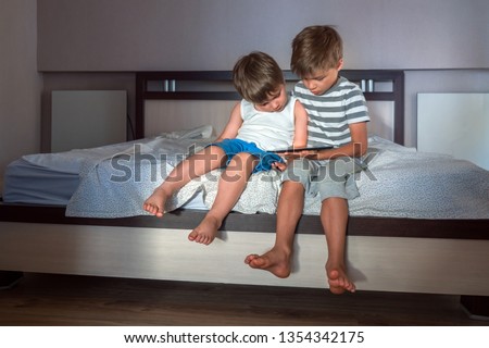 Two boys with ipad sitting on the bed. Generation Z. Children and gadgets background. Kids watching cartoons on tablet. Teens playing games on notebook, notepad. Children and new devices, technologies