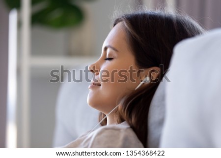 Close up profile view female closed eyes leaned on couch wearing earphones listening music, do meditation visualization dreaming feels happy good. Lazy weekend leisure activities serene person concept Royalty-Free Stock Photo #1354368422
