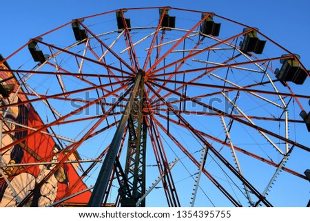 Photo of an antique, red Ferris wheel taken in the daytime looking up toward a blue sky