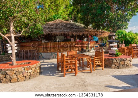 Beach bar with thatched roof, wood and bamboo walls, chairs, beer and glasses. No people, background