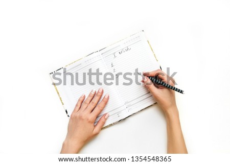Woman's hands with perfect manicure write wishlist with pencil in notebook. White background, flat lay style.