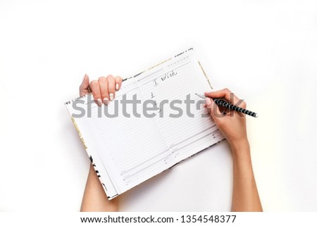 Woman's hands with perfect manicure write wishlist with pencil in notebook. White background, flat lay style.
